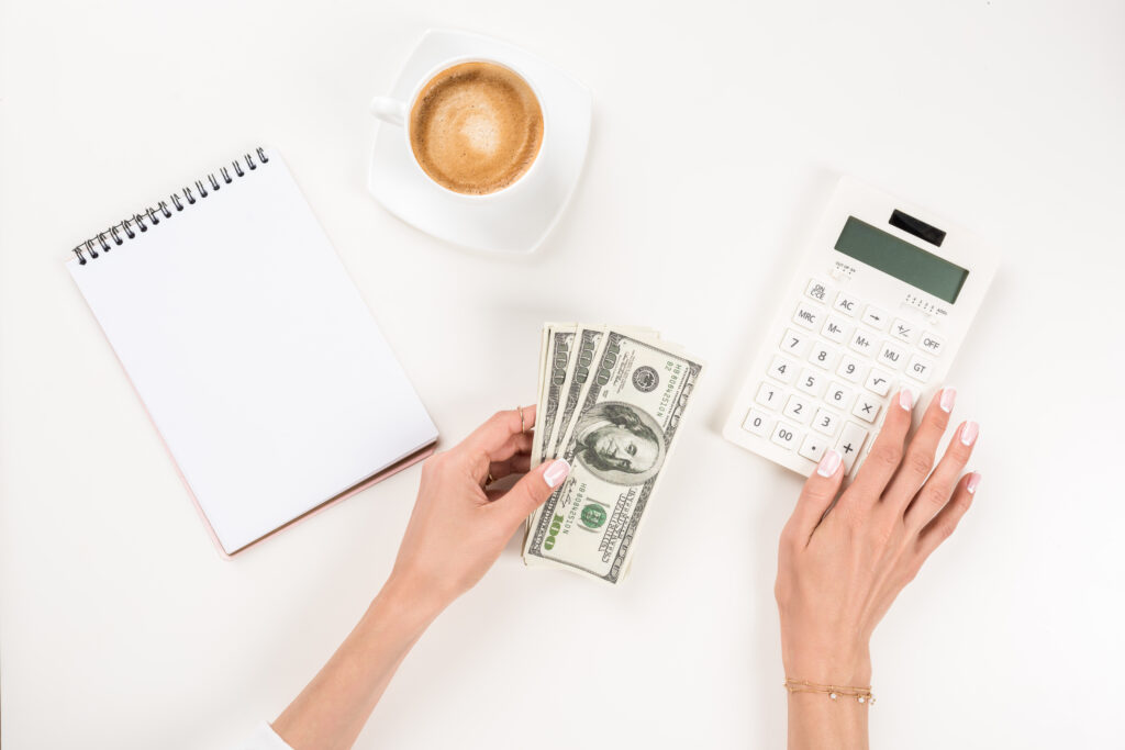 Person calculating finances with cash, calculator, and notepad on white background.